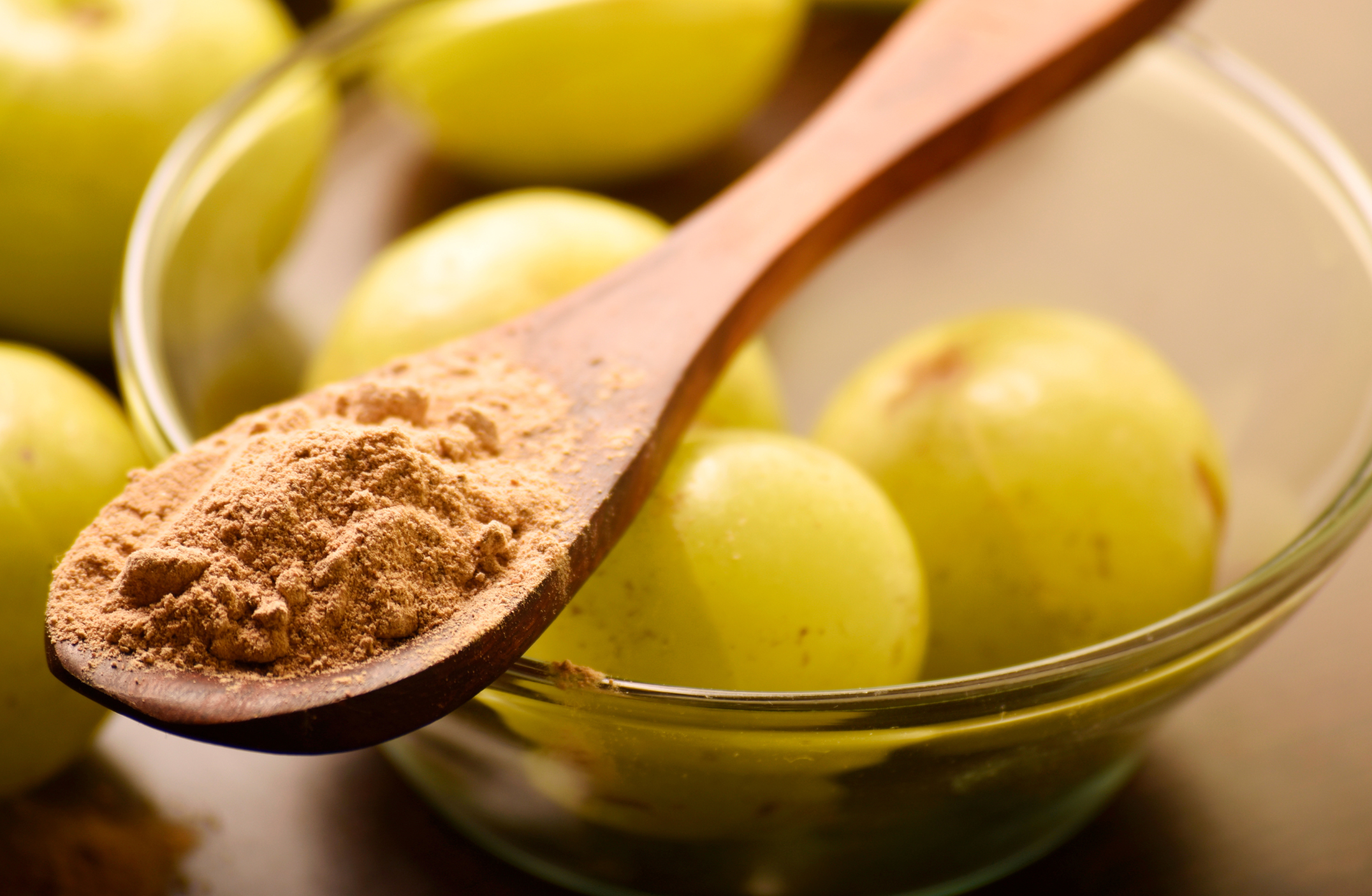 Wooden spoon with amla powder over a bowl of green amla.