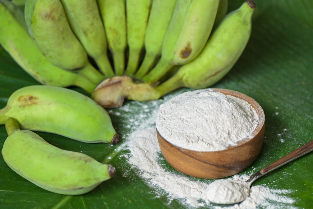 Green Bananas and a bowl full of banana powder on a green leaf